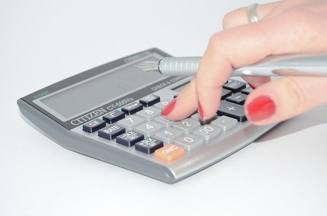 woman with red fingernails holding pen while pressing buttons on calculator