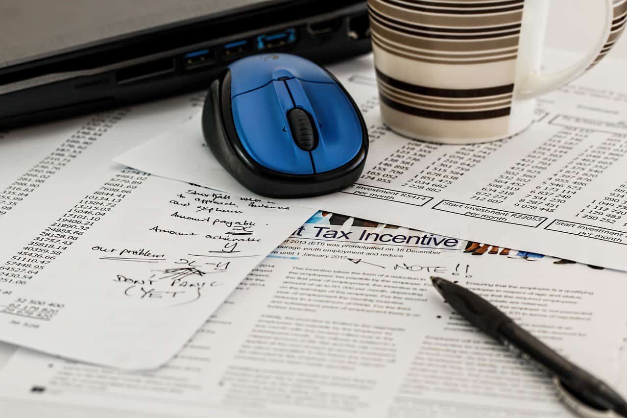 a computer mouse and coffee cup on top of tax paperwork