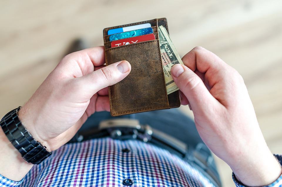 a man pulls folded ten dollar bills out of his leather wallet